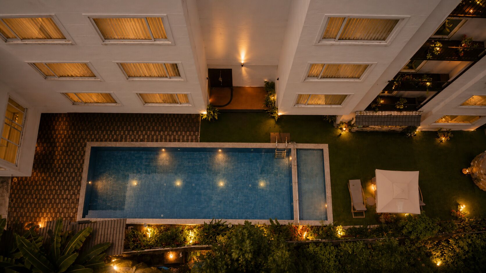An aerial view of a hotel with a swimming pool, multiple balconies, and a well-lit outdoor area.