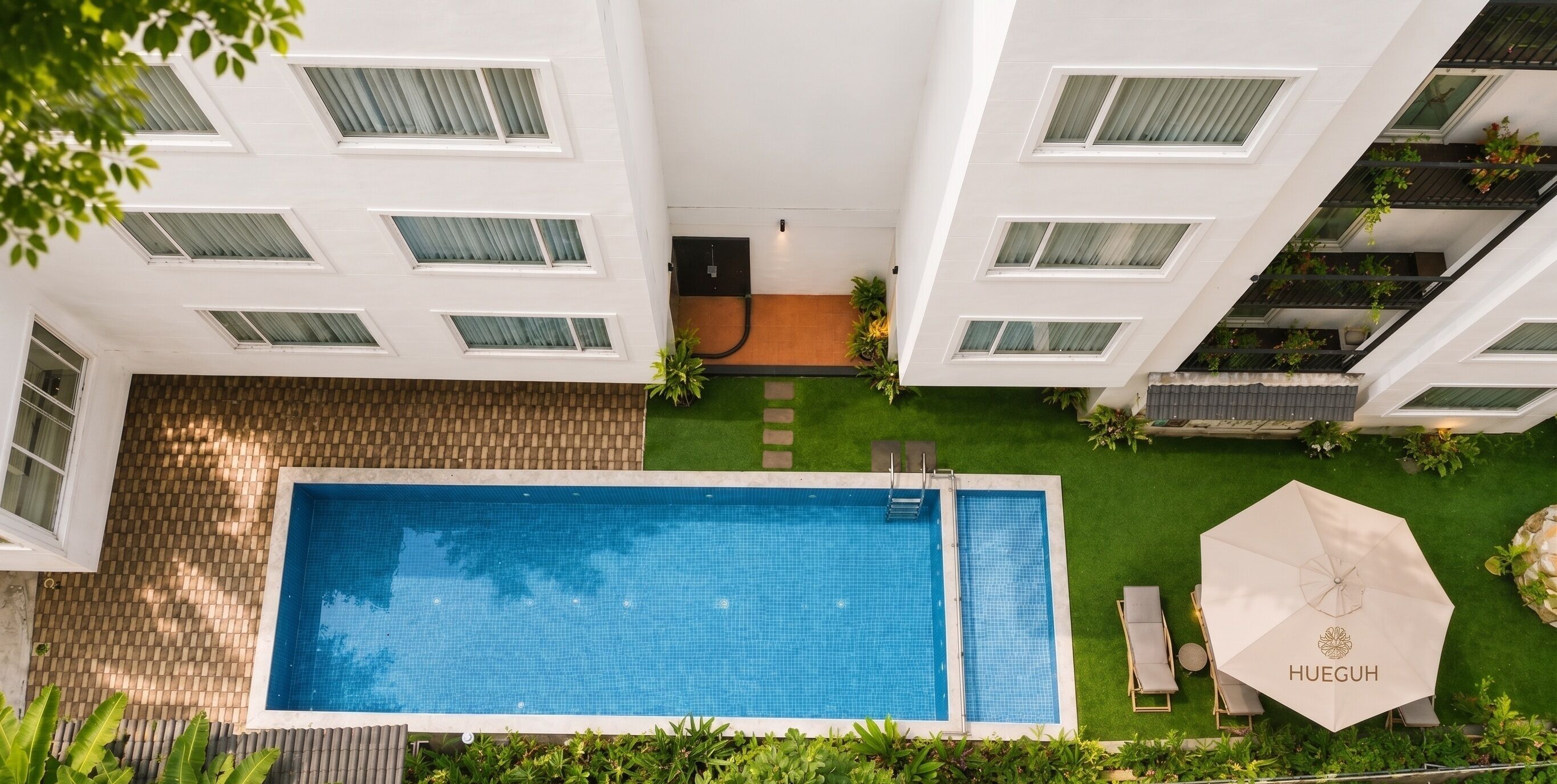 A rooftop pool with a lounge area, surrounded by greenery and a view of the building's architecture.