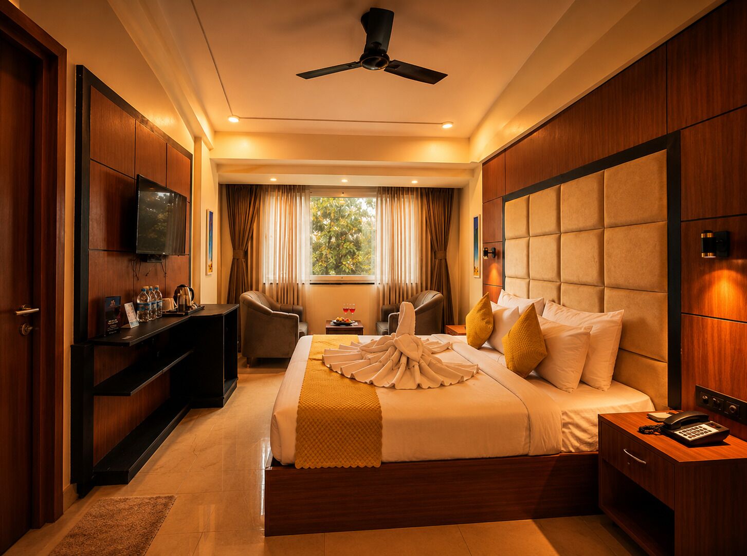 Habitación de hotel con cama, mesita de noche, escritorio, silla, televisor y ventana con cortinas.