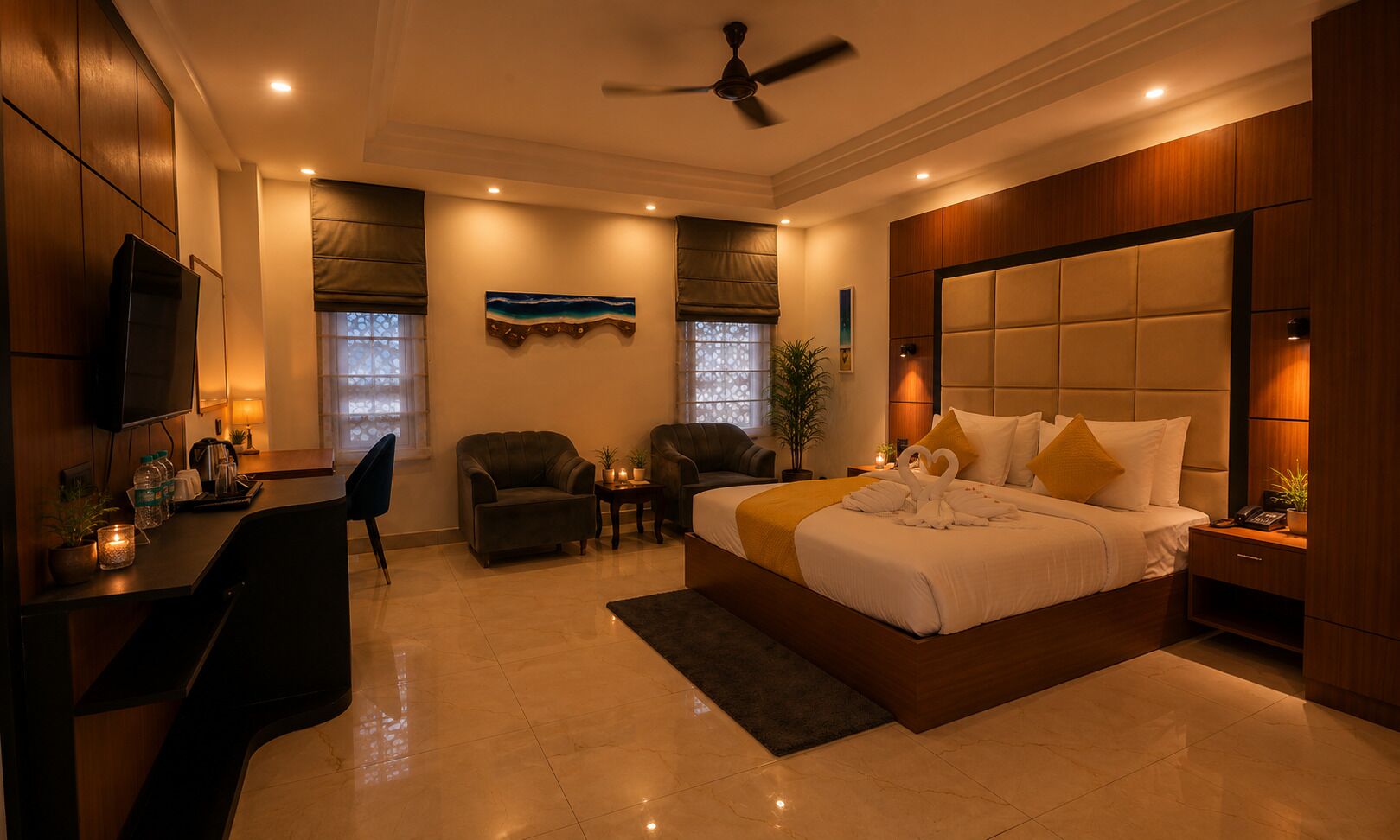 Une chambre d’hôtel avec un lit, deux fauteuils, un bureau, une télévision et un ventilateur de plafond.