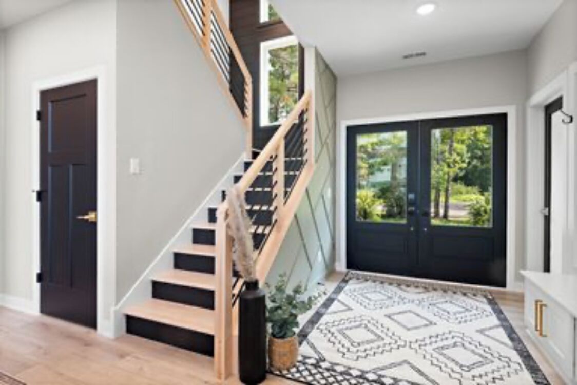 A modern interior with a staircase, a black door, and a patterned rug.