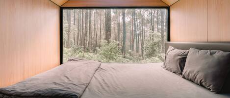 Een slaapkamer met een groot raam, een bed en uitzicht op een bos.