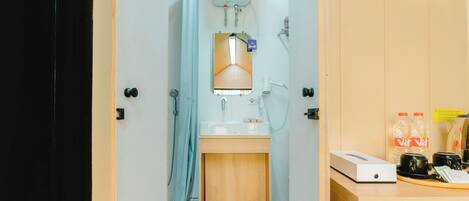 Ein kleines Badezimmer mit Dusche, Waschbecken und Toilette. Ein Bedienfeld befindet sich oberhalb der Dusche, darunter ein kleines Schränkchen.