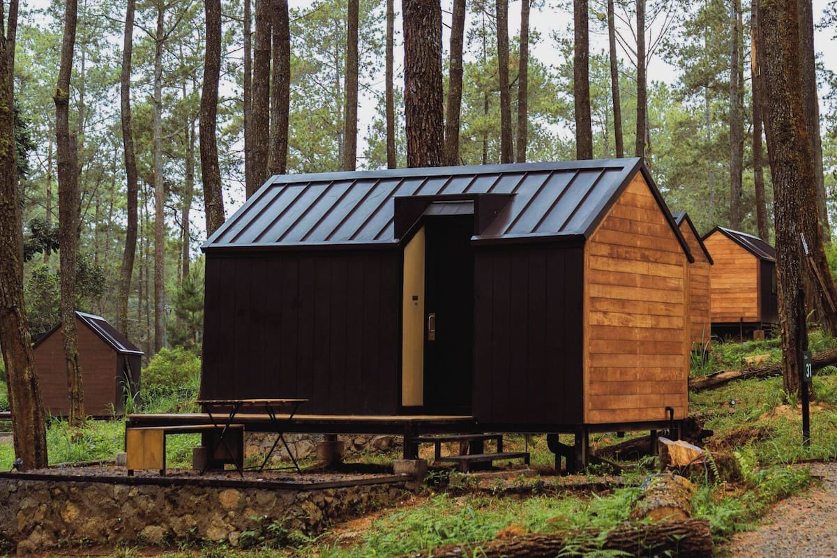 Uma fileira de cabanas de madeira numa floresta, cada uma com telhado inclinado e uma pequena varanda.