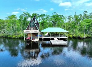 A cabin with a triangular roof, a dock, and a covered area. - Secluded cabin on the water with jetski, hottub & kayak! Pets OK & early checkin (Satsuma)