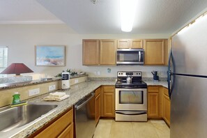 A kitchen with wooden cabinets, a stainless steel refrigerator, an oven, a microwave, and granite countertops.