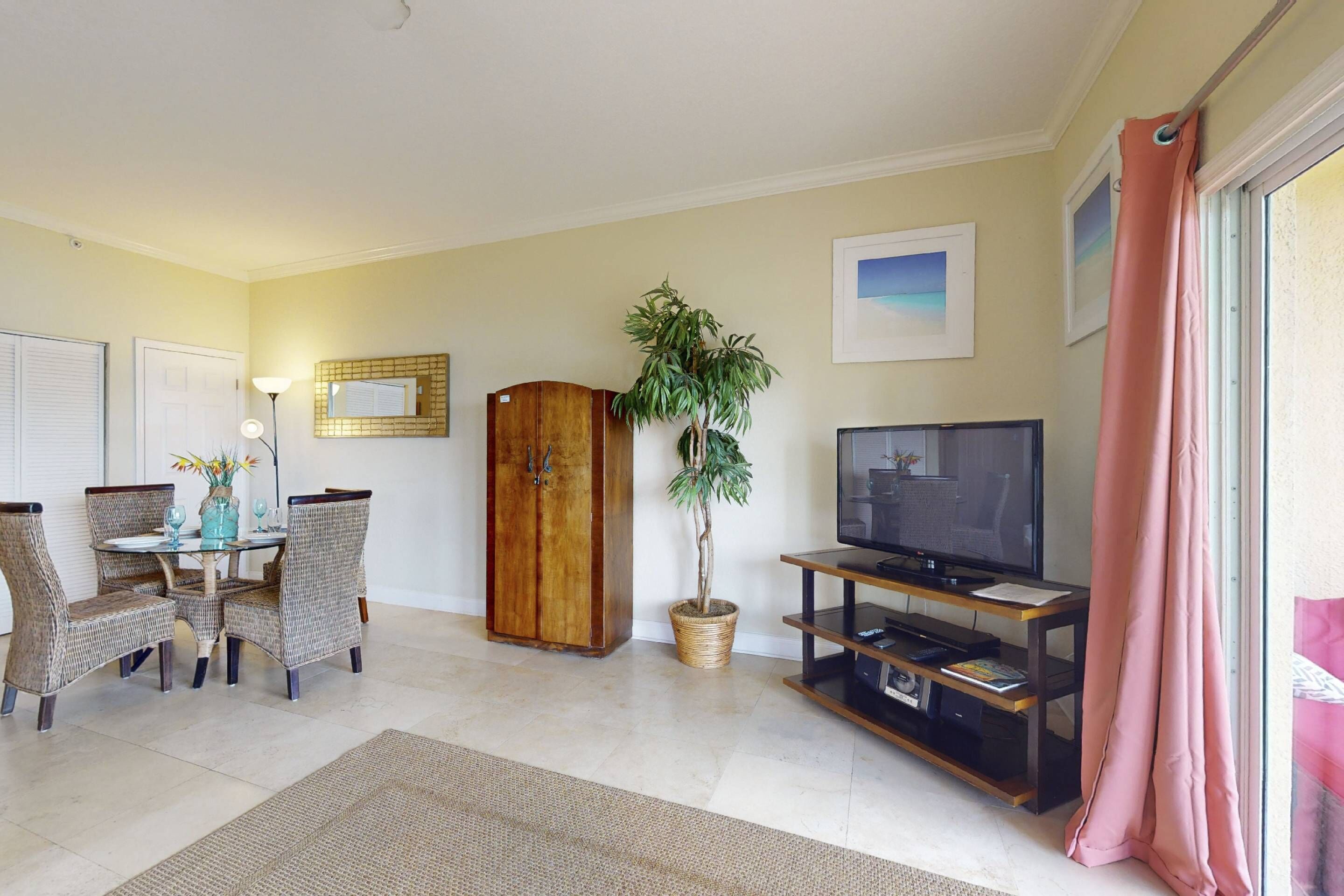 Een woonkamer met een eettafel, stoelen, een televisie, een kast en een potplant.