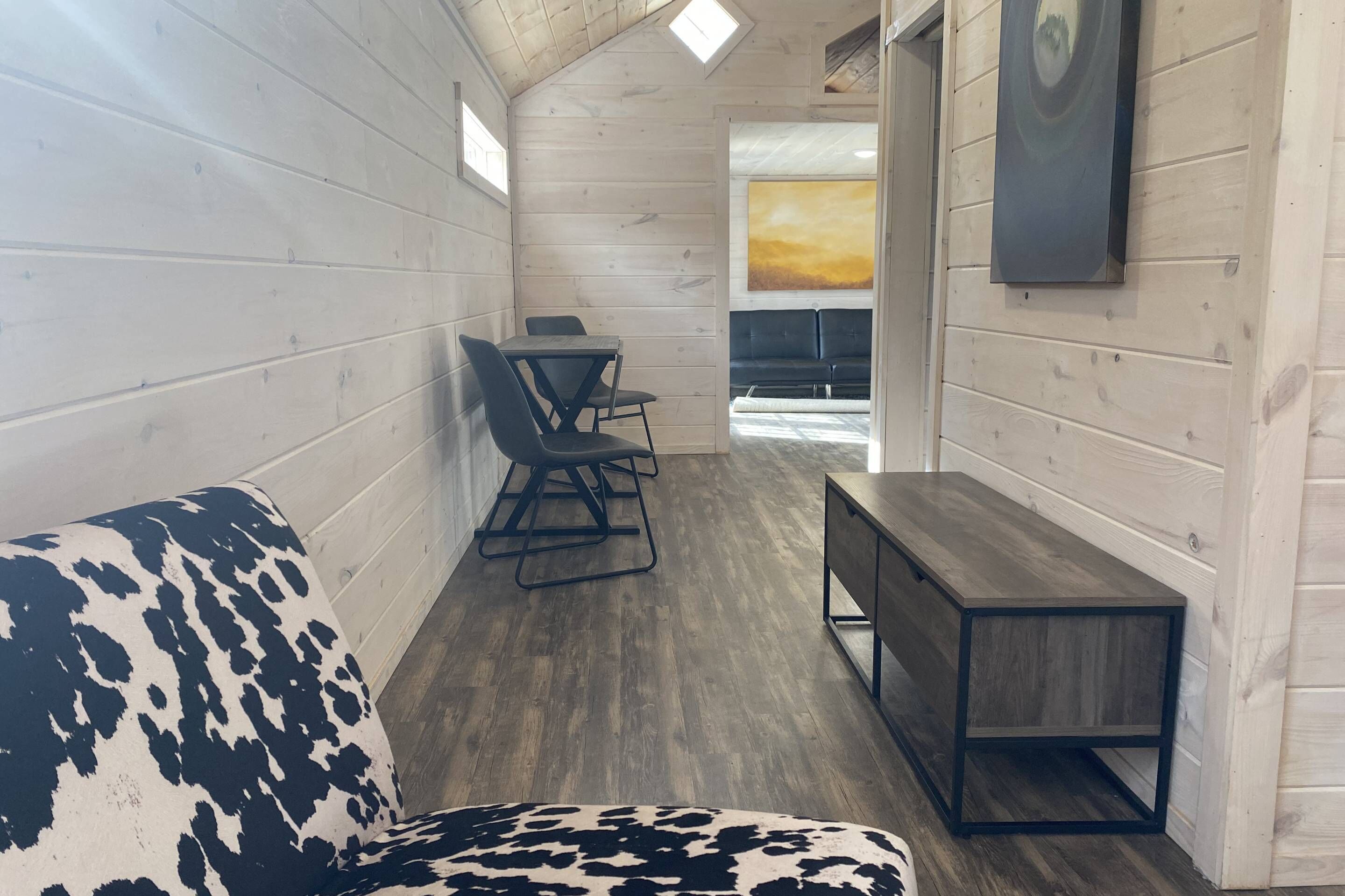 Un intérieur de chalet chaleureux avec un canapé à motifs de vaches, une table à manger avec des chaises et un banc en bois.