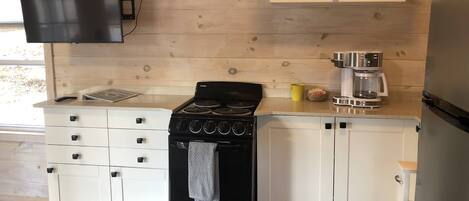 A kitchen with a black stove, white cabinets, a coffee maker, and a flat-screen TV mounted on the wall.