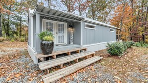 Une petite cabane à un seul étage, dotée d’un porche, d’une pancarte de bienvenue et d’une plante en pot.