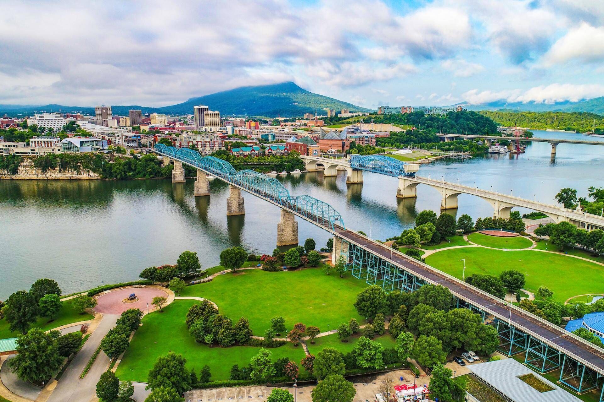 A cityscape with a prominent bridge over a river, surrounded by greenery and urban buildings.