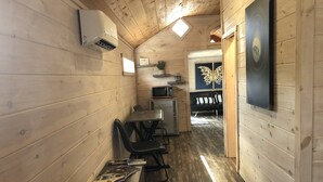 Un couloir étroit aux murs en bois, avec un ventilateur de plafond, un four à micro-ondes, une petite table avec des chaises et un téléviseur fixé au mur.