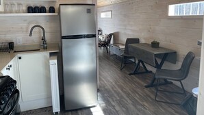 Une cuisine compacte équipée d’un réfrigérateur en acier inoxydable, d’une cuisinière à gaz et d’un évier. Un coin repas avec une table et des chaises est également prévu.
