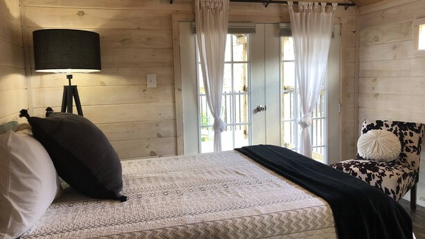 Une chambre à coucher avec un lit, une chaise, une lampe et une fenêtre avec des rideaux.