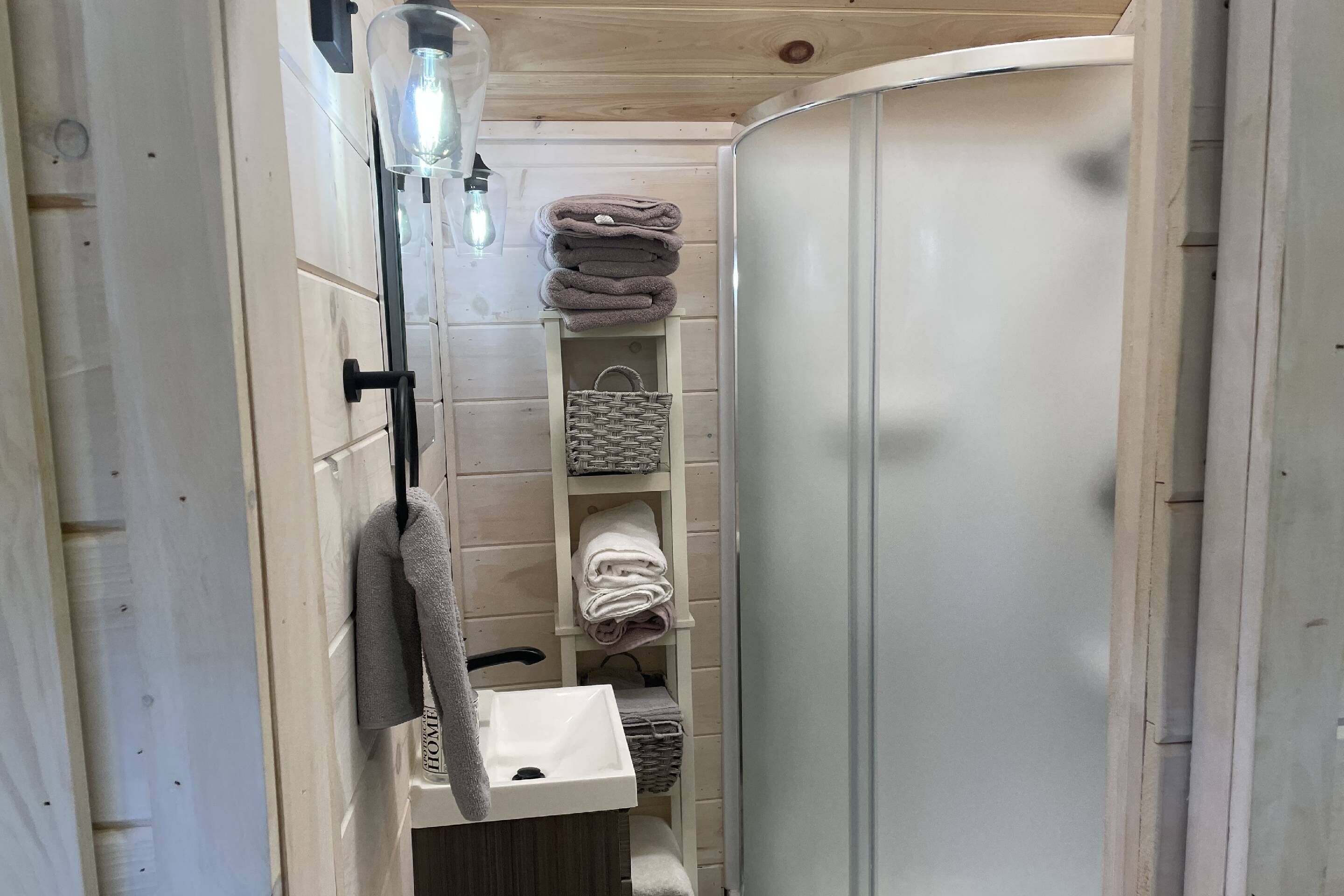 A narrow bathroom with a white sink, a towel rack, and a shelf with folded towels.