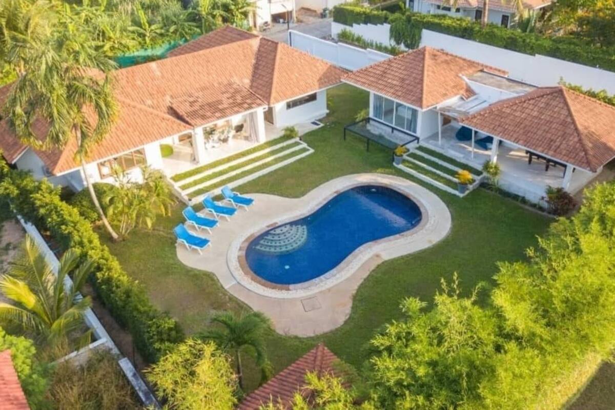 A residential property with a swimming pool, multiple houses, and lush greenery.