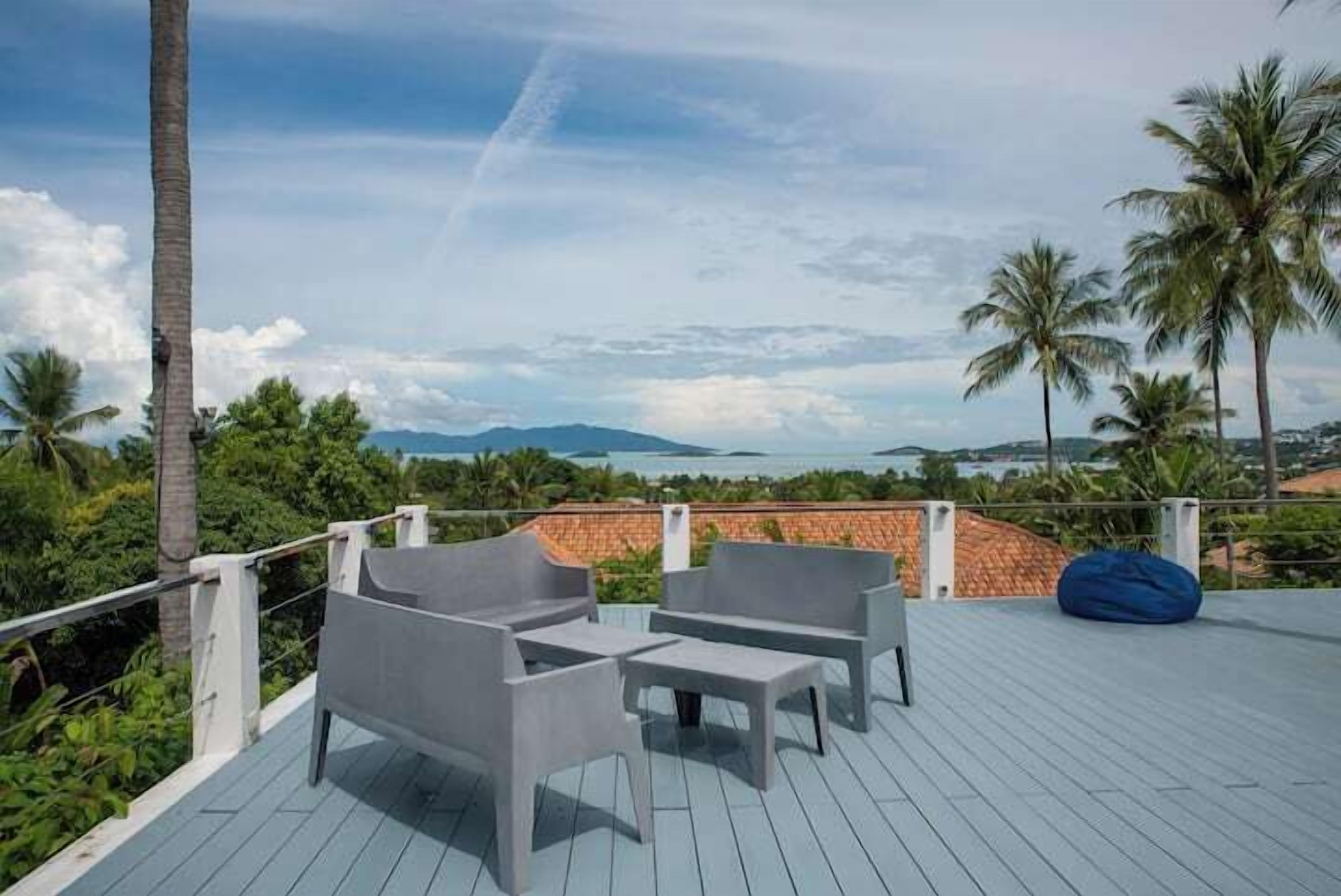 Een terras met buitenmeubilair, een blauwe loungestoel en uitzicht op zee en bergen.