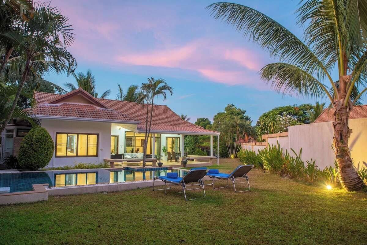 A modern house with a swimming pool, lounge chairs, and palm trees.