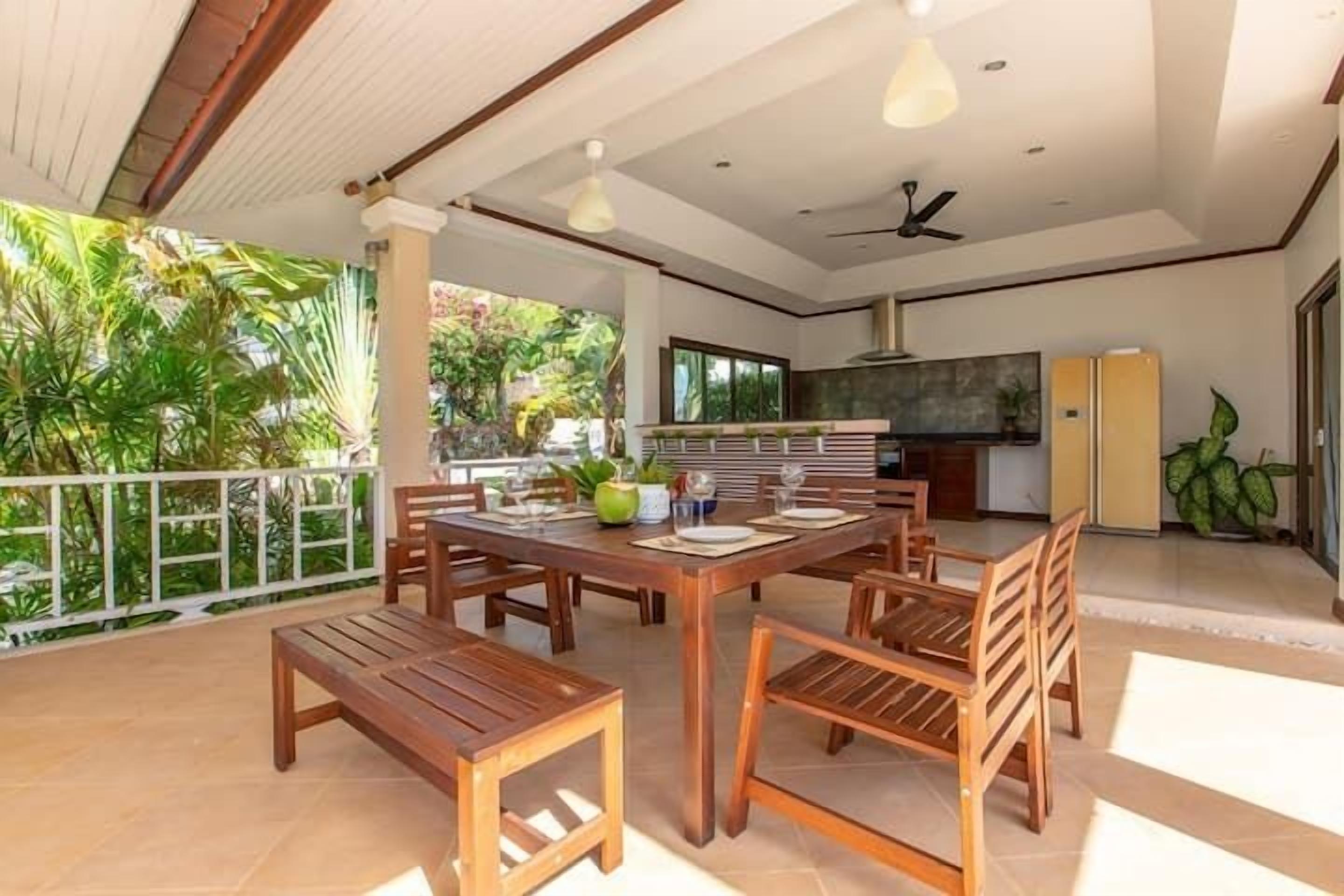 An open-plan living area with a dining table and chairs, a kitchen area, and a balcony with a view of greenery.