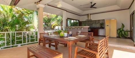 An open-plan living area with a dining table and chairs, a kitchen area, and a balcony with a view of greenery.
