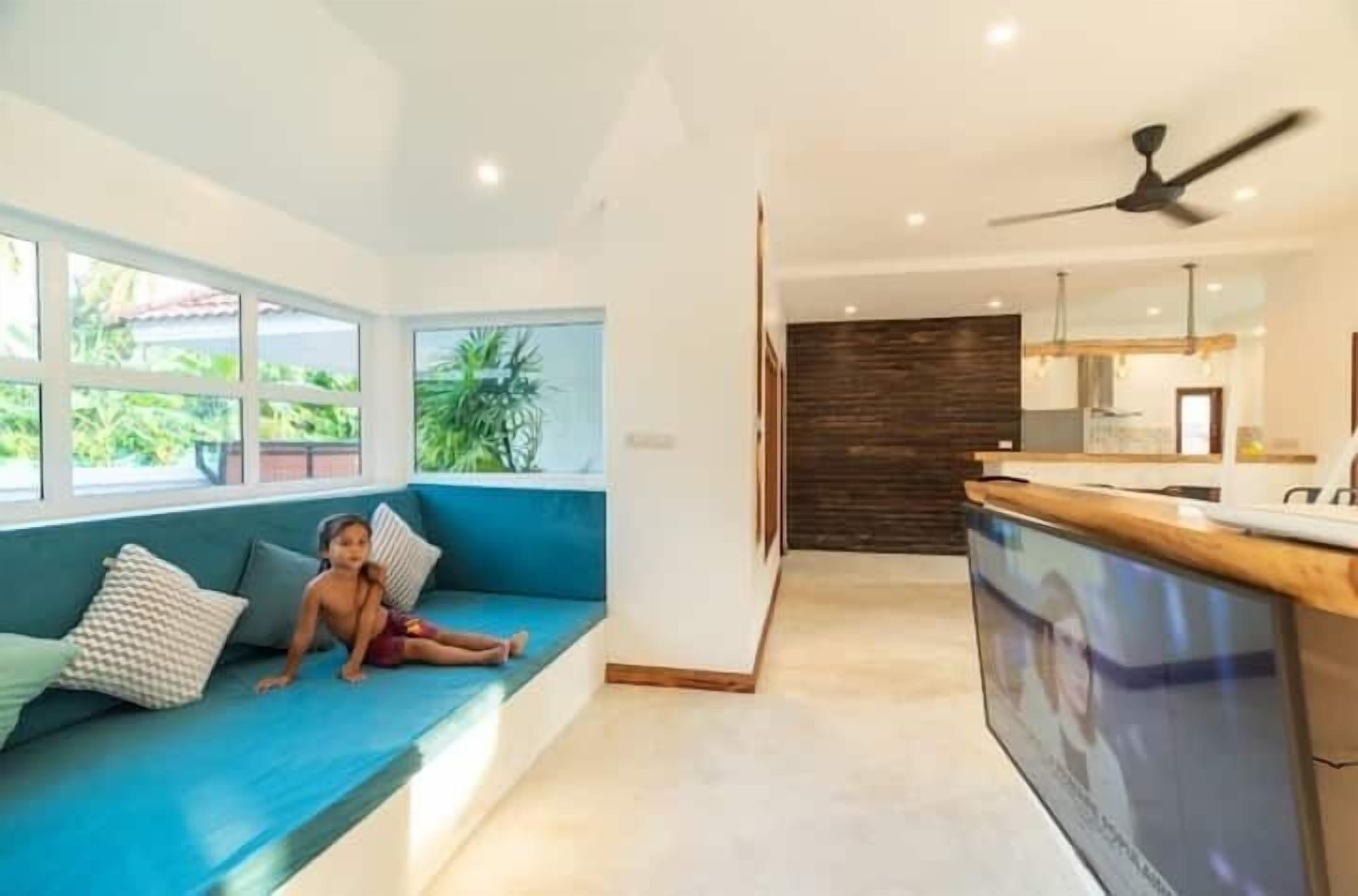 Una sala de estar moderna con un sofá azul, una zona de cocina y un ventanal con vistas a zonas verdes.