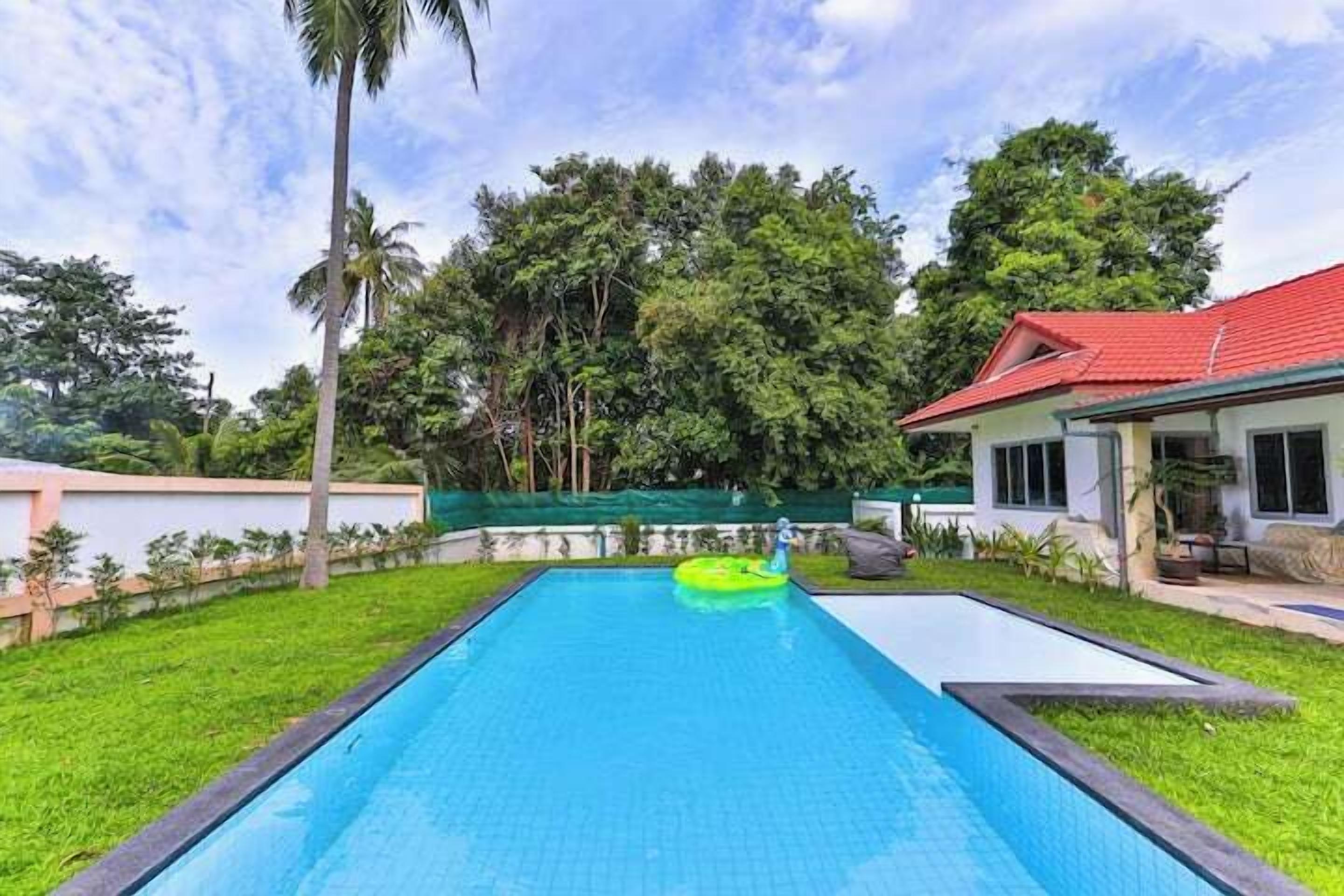 Una piscina con un flotador inflable verde, rodeada por un césped cuidado y una casa con techo rojo.