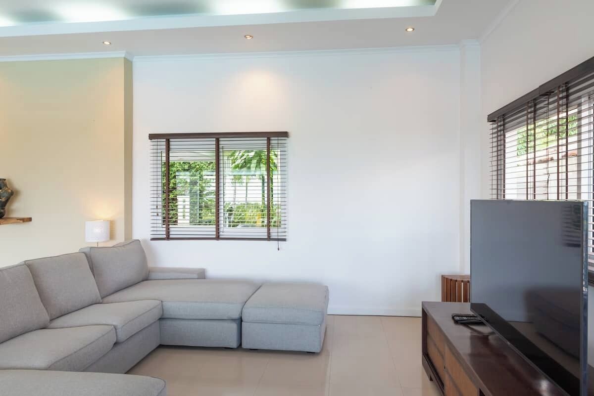 Een moderne woonkamer met een hoekbank, een flatscreen televisie en een raam met jaloezieën.
