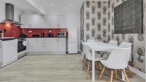 A modern kitchen with white cabinets, a red backsplash, and a dining area with a white table and chairs. - We Stay - Baxter Gate (Loughborough)