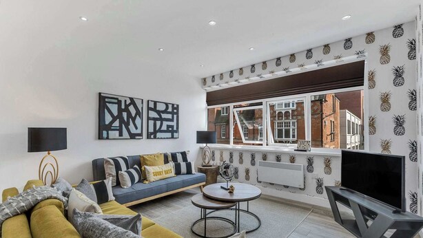 A modern living room with a sofa, coffee table, and TV, featuring abstract wall art and a pineapple-patterned wall. - We Stay - Baxter Gate (Loughborough)