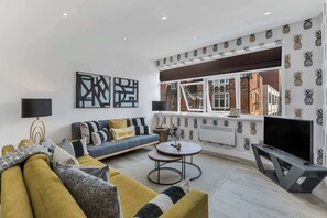 Una sala de estar moderna con sofá, mesa de centro y televisor, con arte abstracto en la pared y un diseño de piña en la pared.