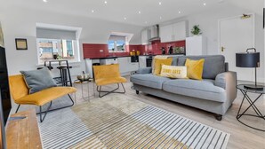 A modern living room with a sofa, chairs, a coffee table, and a kitchen in the background. - We Stay - Baxter Gate (Loughborough)