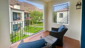Un balcon agrémenté de meubles en osier, une vue sur un jardin et un bâtiment doté d’un toit en tuiles.