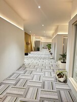 A hallway with patterned flooring, potted plants, and recessed lighting.
