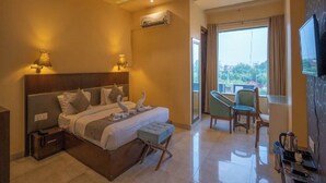Habitación de hotel con cama, mesitas de noche, escritorio, silla, televisor y balcón con vistas.