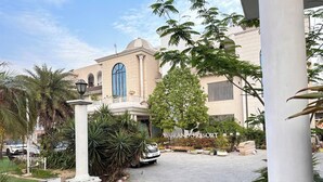 Entrada de un resort con un camino pavimentado, palmeras y un edificio con cúpula y ventanas arqueadas.