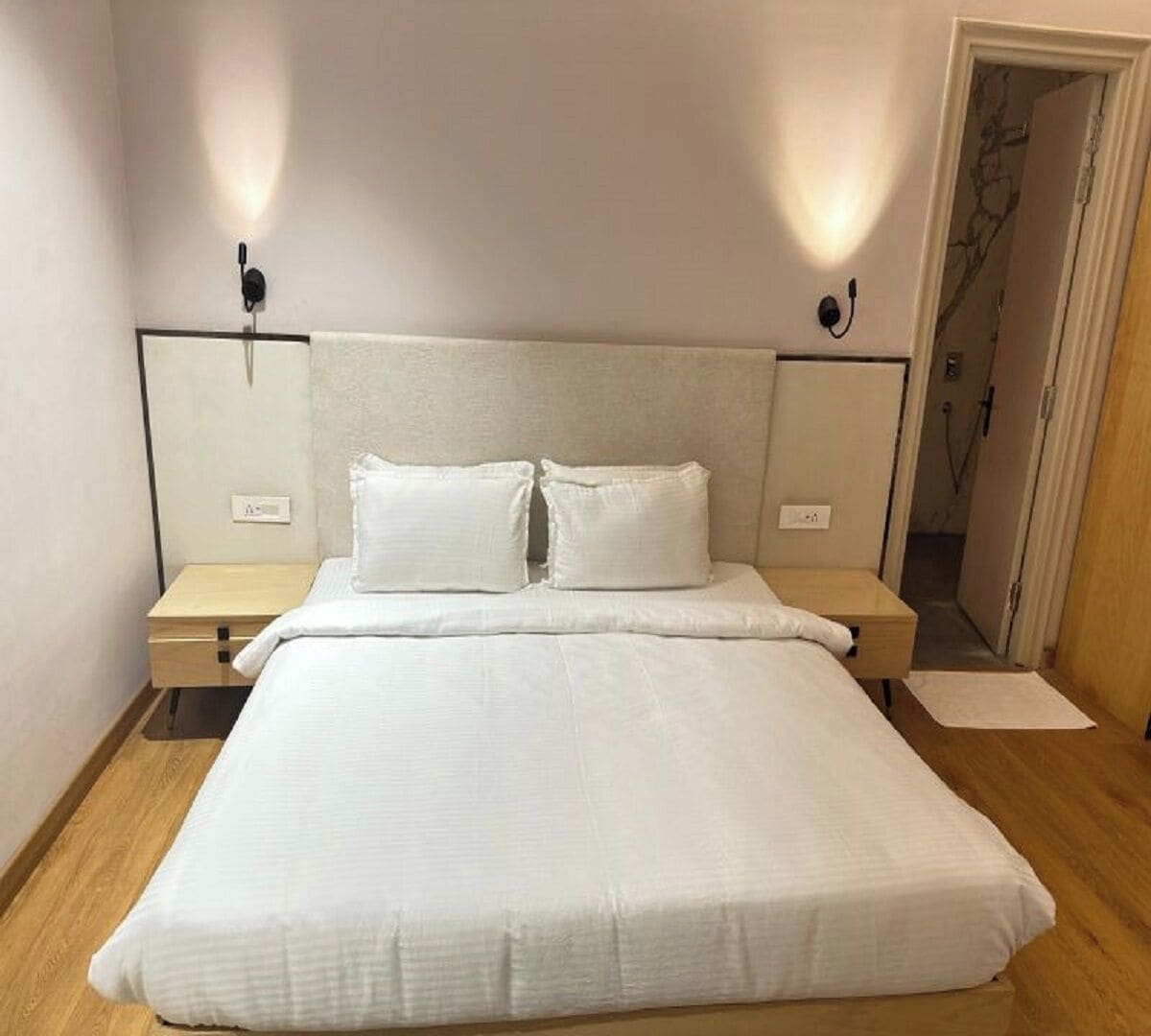 A neatly made bed with white bedding, two bedside tables, and wall-mounted lamps.
