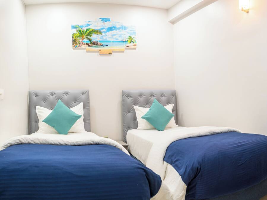 Une chambre avec deux lits, chacun doté d’une tête de lit grise et d’oreillers turquoise, et une œuvre d’art sur le thème de la plage accrochée au mur.