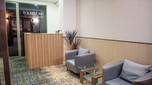 Eine Lobby mit einer Rezeption, zwei grauen Sofas, einem Glastisch und einem gemusterten Teppich.