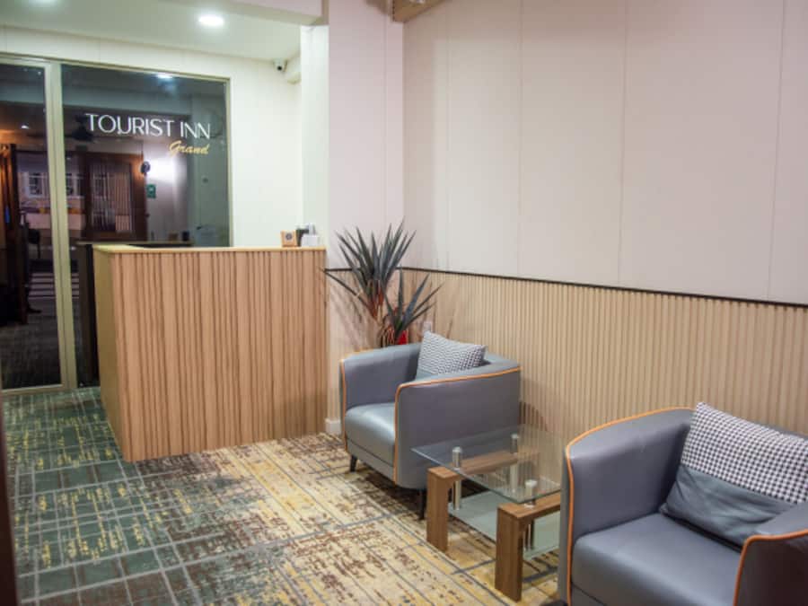 A lobby with a reception desk, two grey sofas, a glass coffee table, and a patterned carpet.