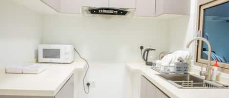 A compact kitchen with a microwave, kettle, and sink.