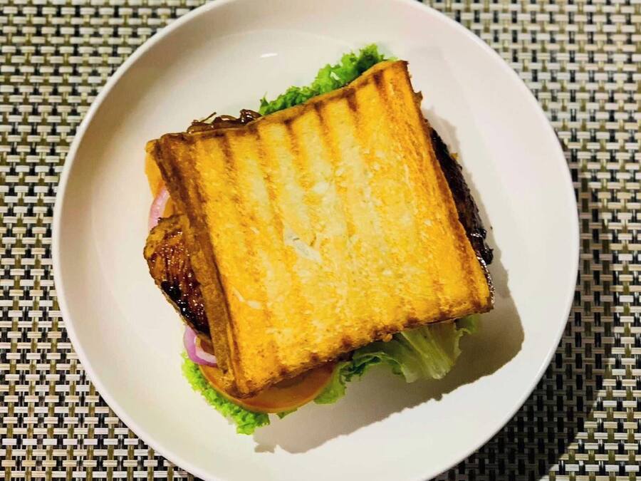 Un sándwich sobre un plato blanco con lechuga y una rebanada de pan a la plancha.