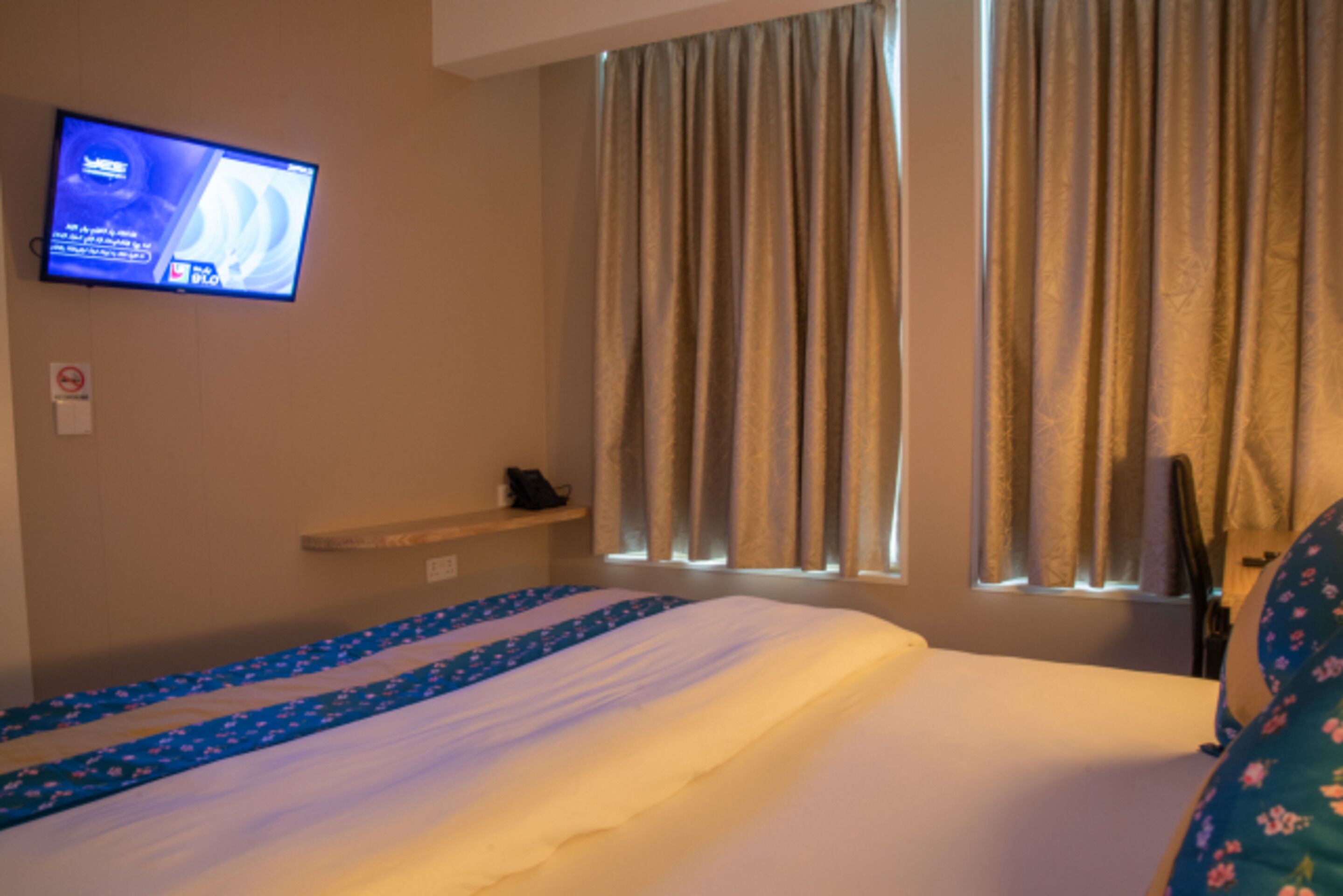 Une chambre d’hôtel avec un lit, un téléviseur fixé au mur et une fenêtre avec des rideaux.