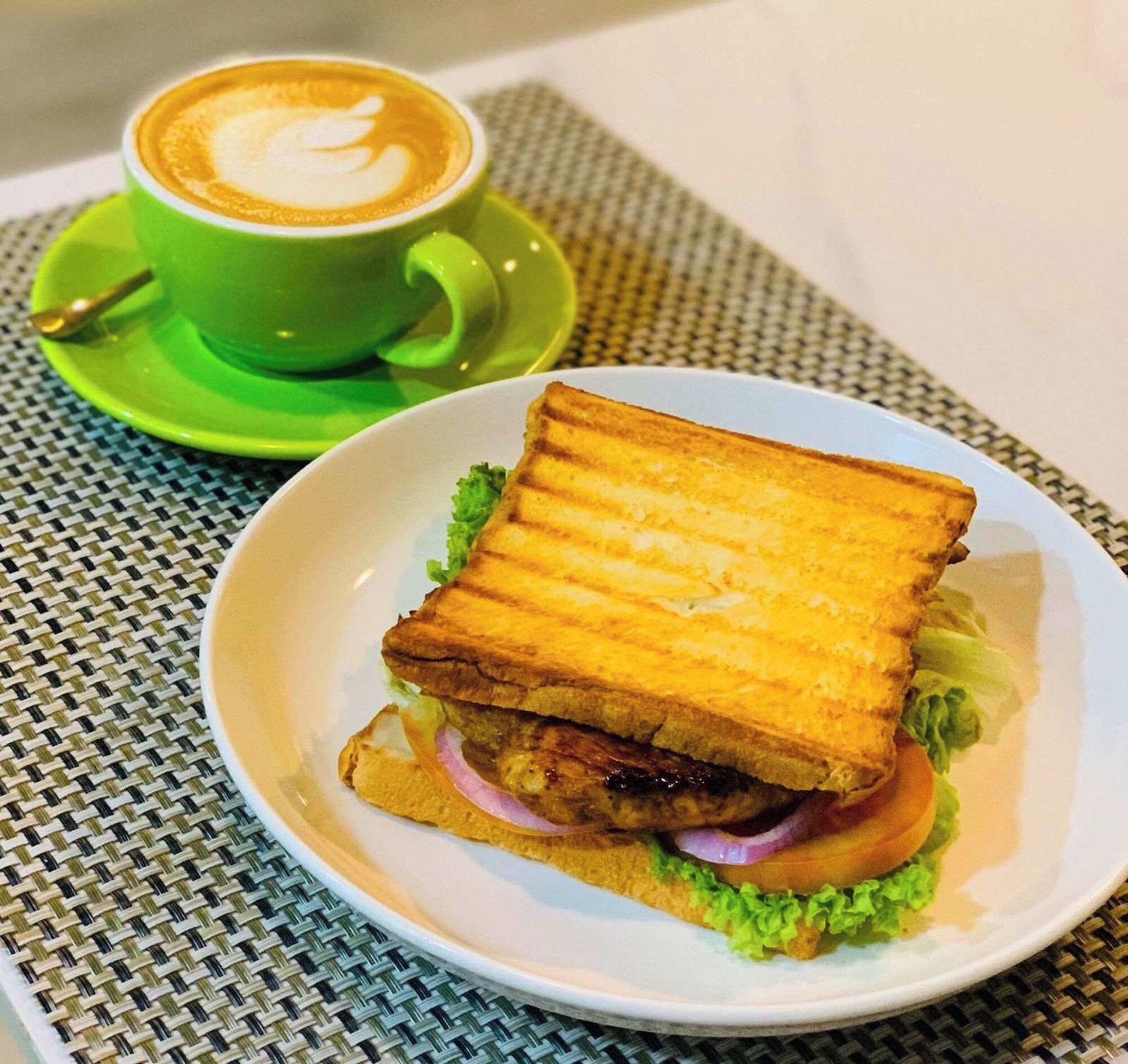 En sandwich med salat, løg og et stykke kød, serveret på en hvid tallerken.