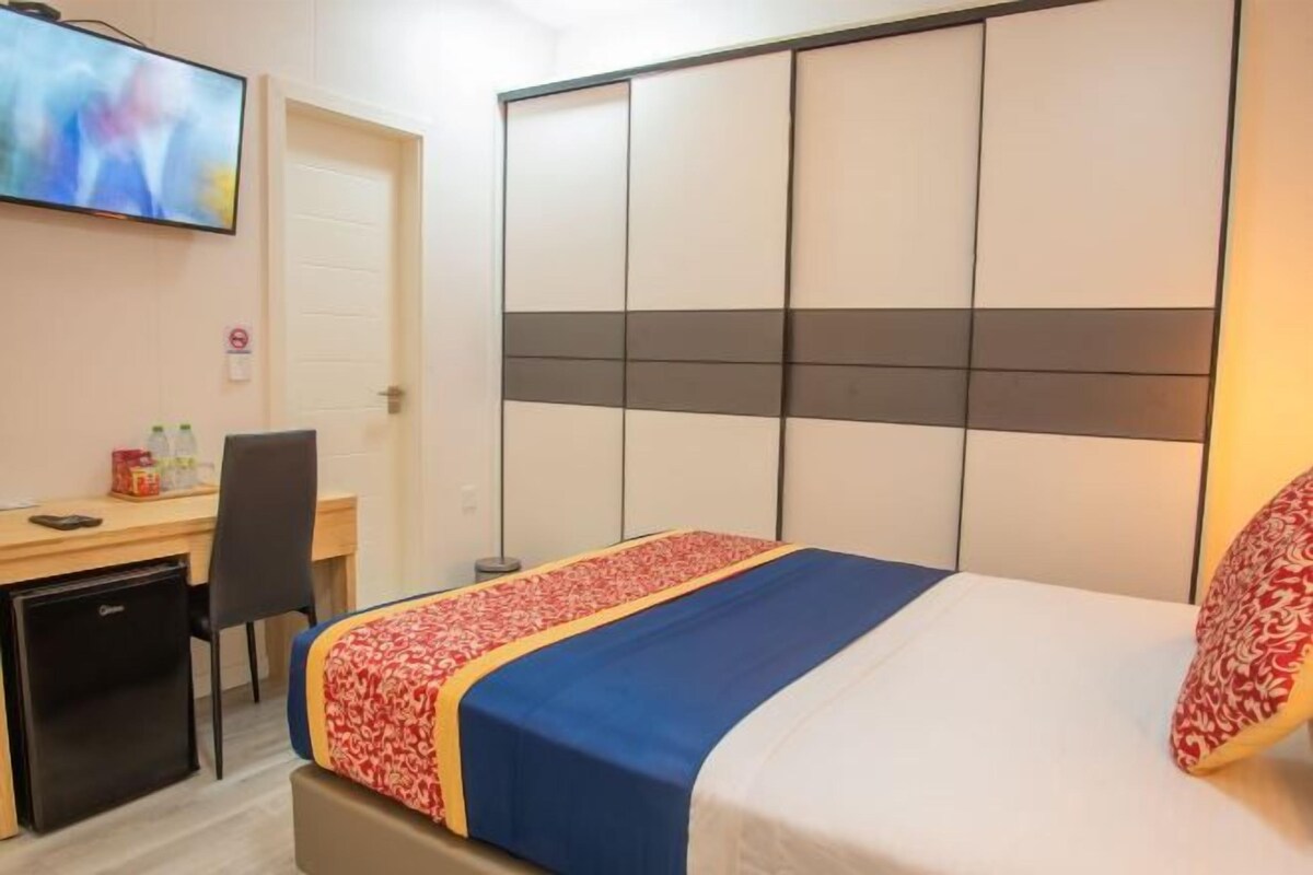 Ein Hotelzimmer mit einem Bett, einem Schreibtisch mit Computer, einem Kühlschrank und einem Fernseher an der Wand.
