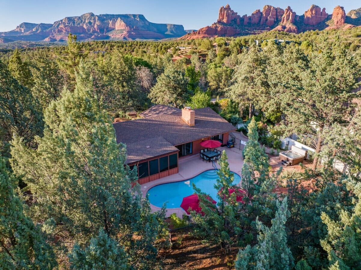A house with a swimming pool surrounded by trees, with a view of red rock formations in the background.
