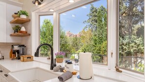 Une cuisine moderne avec des meubles blancs, une grande fenêtre et une vue sur les arbres et les montagnes.