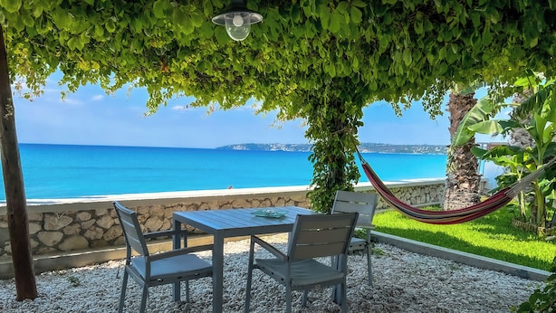 Une terrasse avec une table et des chaises, un hamac et une vue sur la mer.