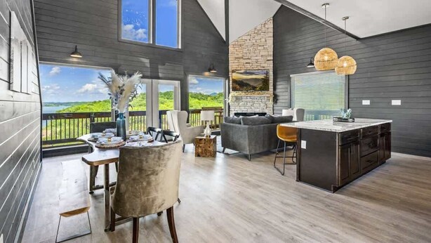 A spacious living area with a large window, a fireplace, and a dining area with a table and chairs. - Luxe at Lake Haven - Lakefront pool & hot tub (Sevierville)