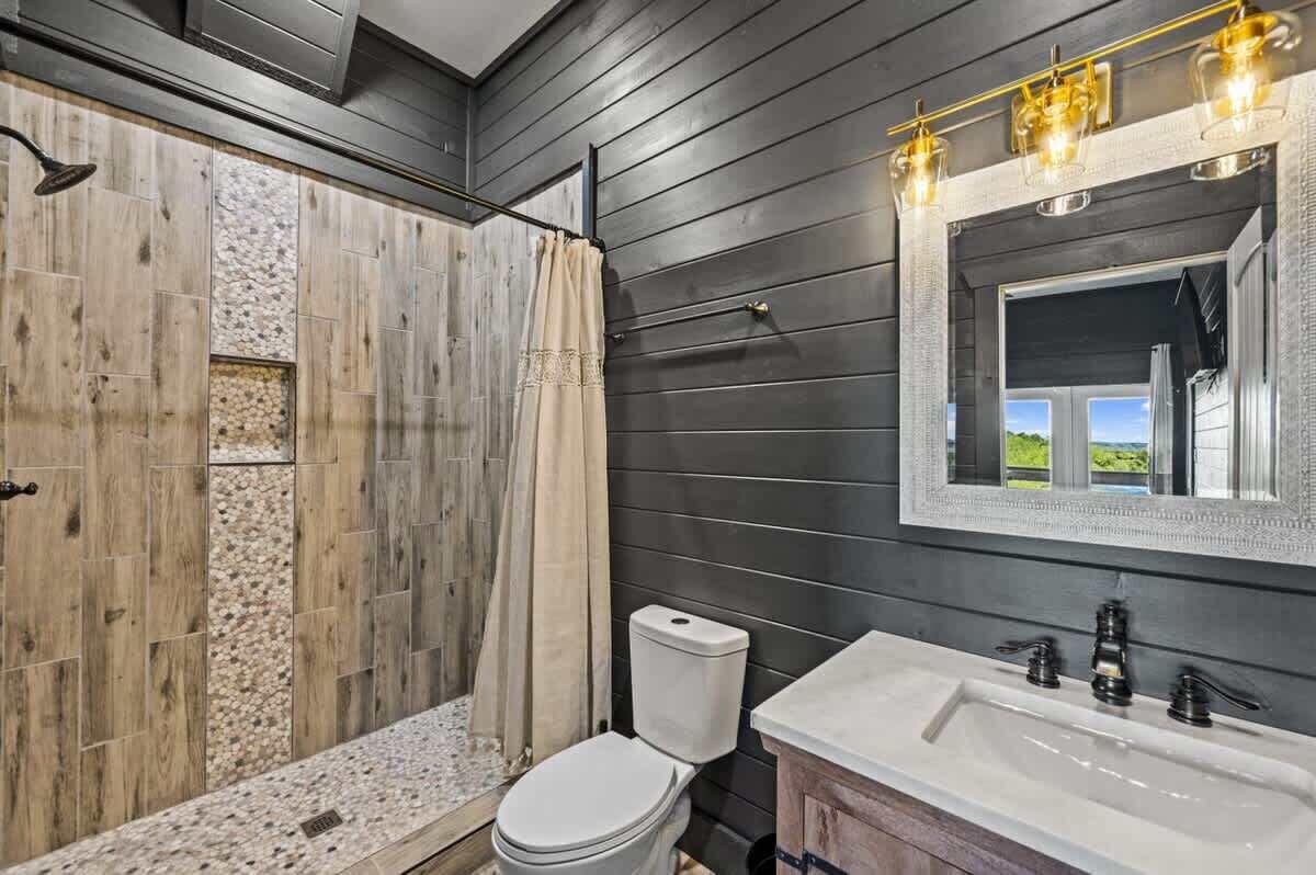Ein Badezimmer mit Duschkabine aus Holz, Toilette, Waschbecken mit Spiegel und Fenster mit Ausblick.