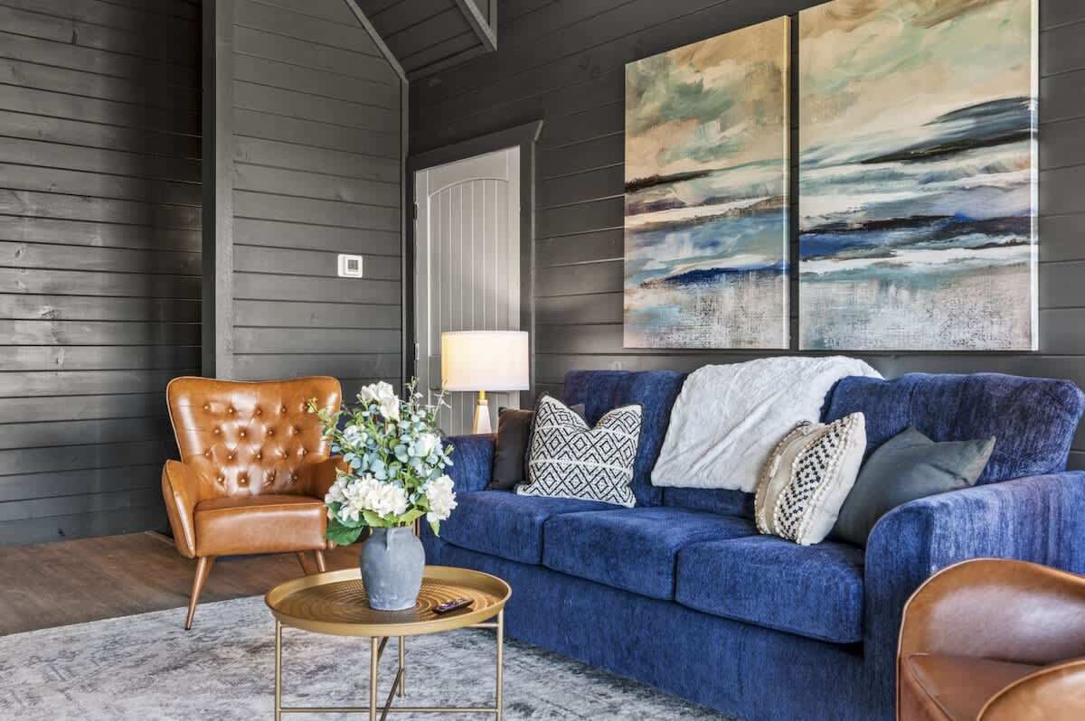 Ein Wohnzimmer mit einem blauen Sofa, einem Ledersessel, einem runden Couchtisch und einer Blumenvase.